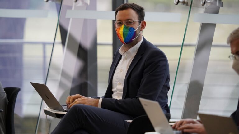 Daniel mit Laptop und Atemmaske in Regenbogenoptik sitzend im sächsischen Landtag