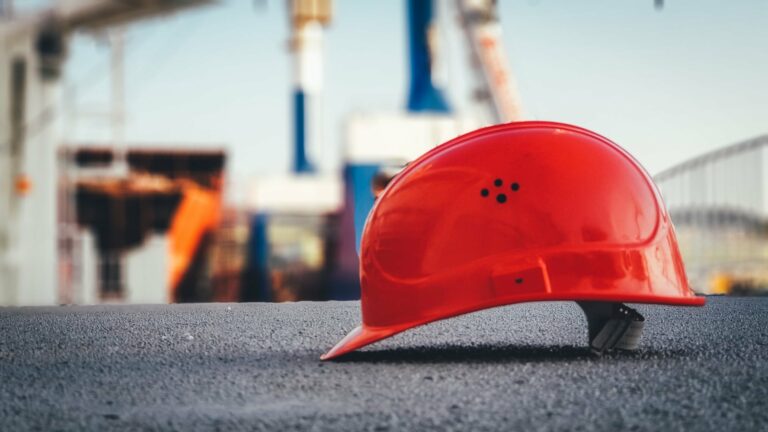 Roter Bauhelm auf Asphalt liegend mit Baustelle im Hintergrund