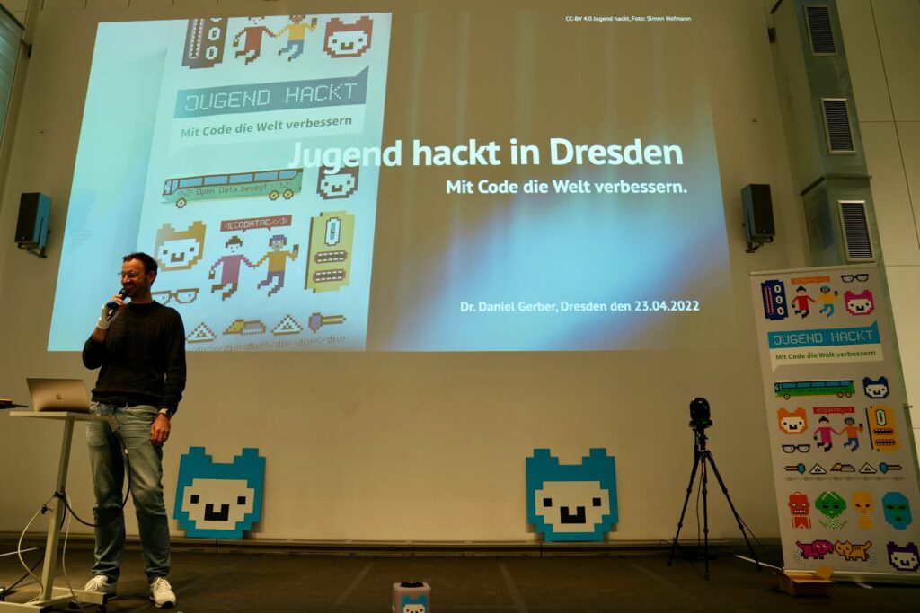 Daniel auf der Bühne bei Jugend hackt mit seinem Vortrag im Hintergrund auf der Leinwand