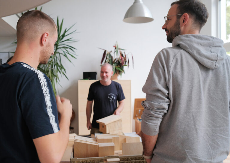 Zu sehen sind Daniel und ein Workshop-Teilnehmer in Rückenansicht in der Mitte steht Karsten und zeigt etwas