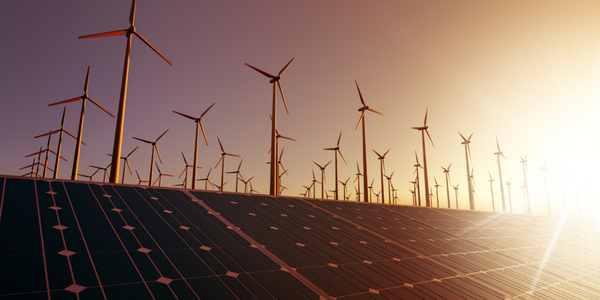 Photovoltaikmodule und Windräder im Hintergrund während eines Sonnenuntergangs.