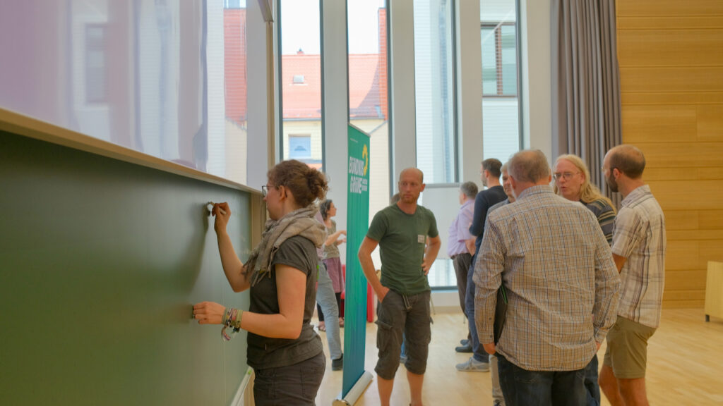 Lea Fränzle notiert an einer Tafel Ideen der Workshopteilnehmer:innen.