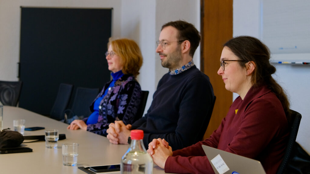 Tabea Rößner, Daniel Gerber und Claudia Maicher sitzen am Tisch und schauen die Redner:innen an.